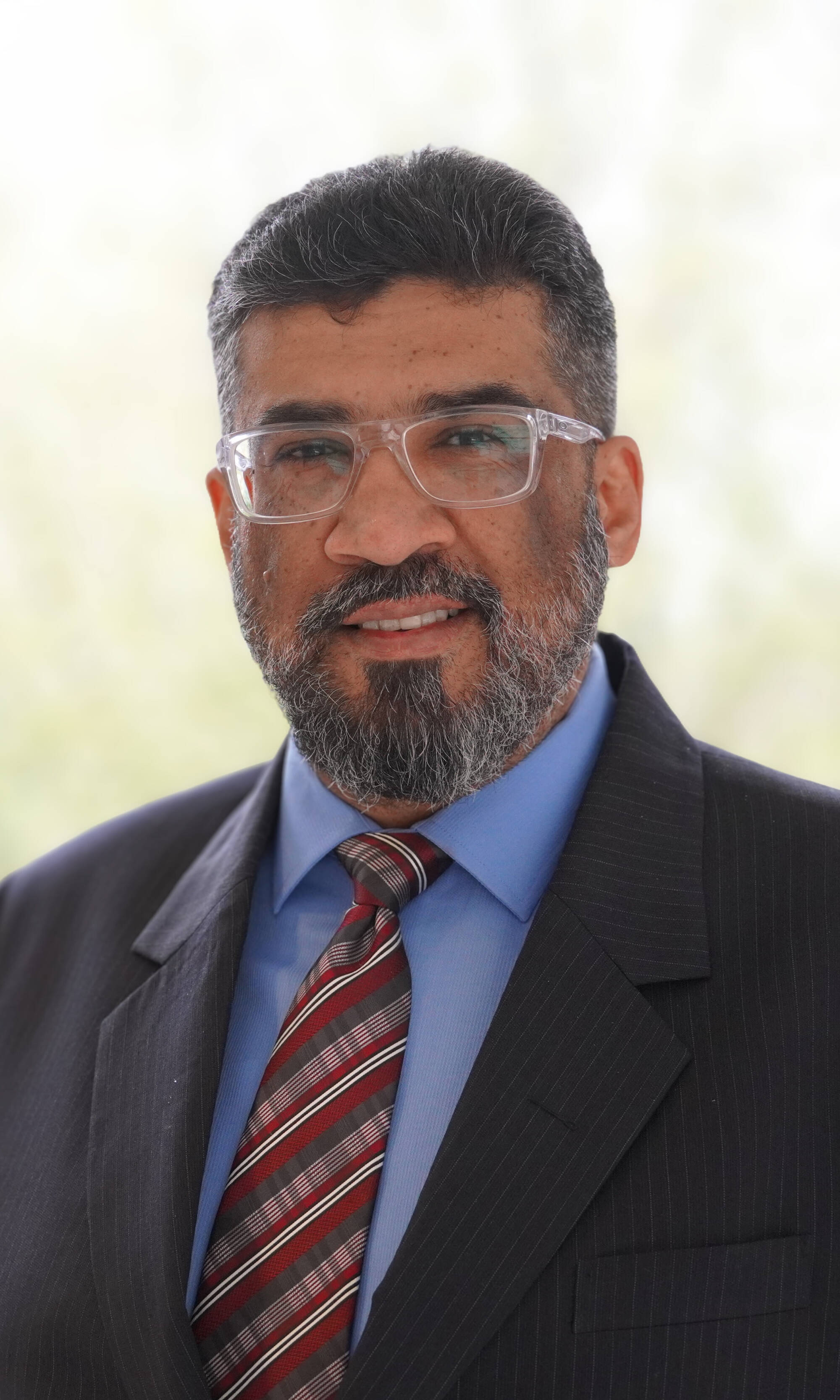 Dr. Samir Iqbal smiling at the camera while wearing a suit in a professional setting.